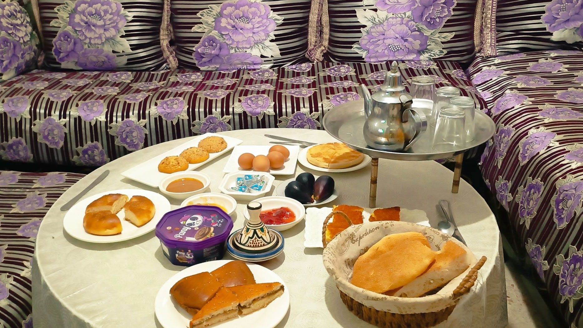 The shared lounge at Aziz House, with Moroccan banquette seating around a table laid for breakfast